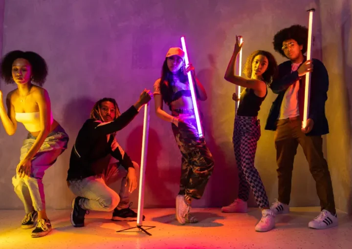 A group of young adults holding neon lights in a darkened room