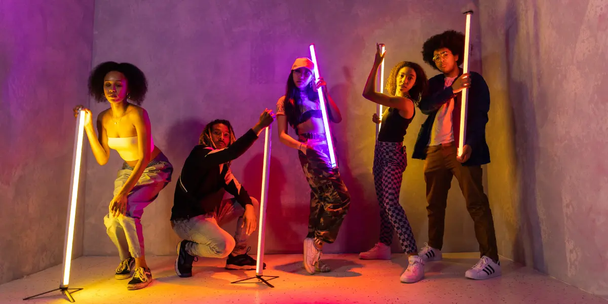 A group of young adults holding neon lights in a darkened room